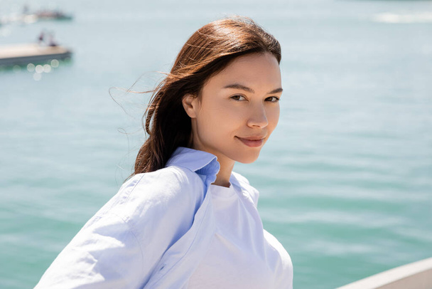 portrait of positive brunette woman looking at camera near sea - Zdjęcie, obraz
