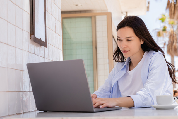 brunette woman in blue shirt working on laptop in street cafe - Фото, изображение