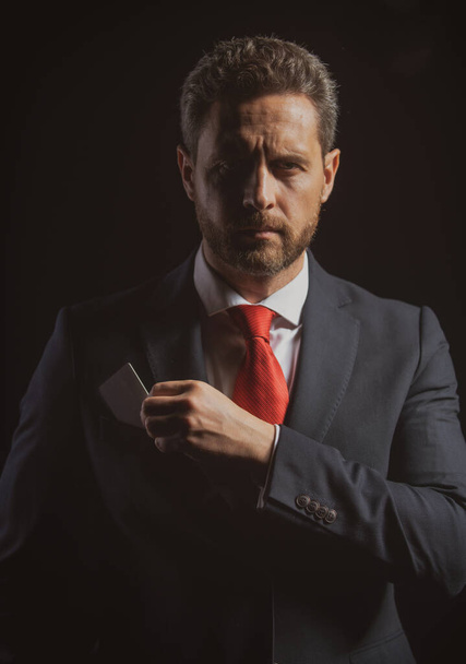 Portrait of an elegant handsome business man isolated on black. Handsome thoughtful middle-aged businessman with credit card in suit posing against a black background with copy space. - Photo, image