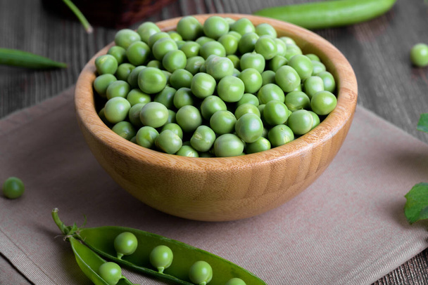 Fresh organic raw green peas in a bowl with peas plants leaves on dark wooden table background. Healthy eating, vegan and vegetarian legume food, raw food and detox super food, bean protein, close up - Photo, Image