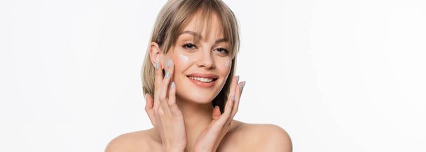 happy woman with bangs applying cream on cheeks and looking at camera isolated on white, banner - Foto, immagini