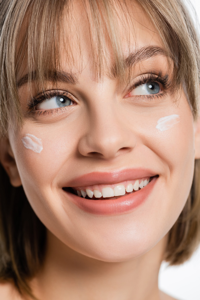close up of happy woman with bangs and cream on cheeks isolated on white - 写真・画像