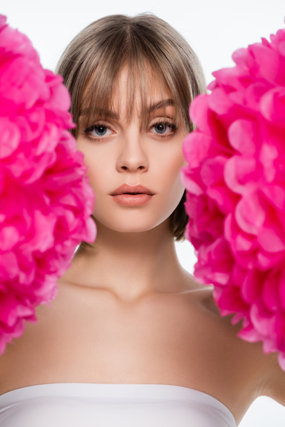young woman with blue eyes looking at camera through blurred pink flowers isolated on white - Foto, Imagen