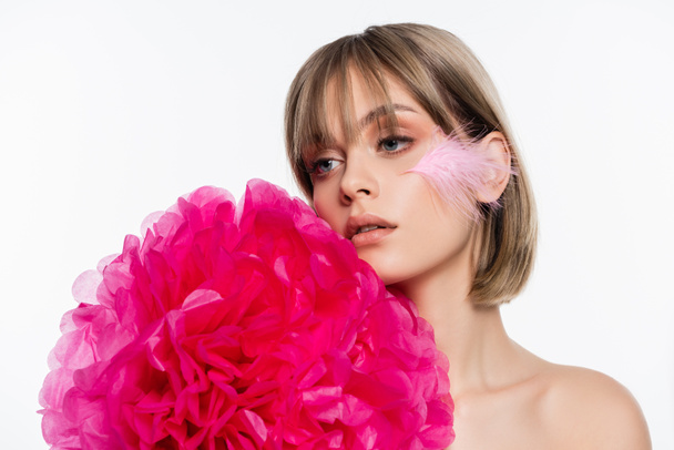young woman with feather on cheek near bright pink decorative flower isolated on white - Photo, Image