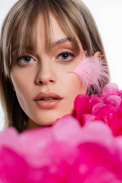 pretty young woman with feather on cheek near blurred pink decorative flowers isolated on white - Foto, Imagen