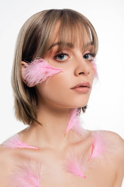 young woman with decorative elements on face and body and pink feathers on cheeks isolated on white - Fotó, kép
