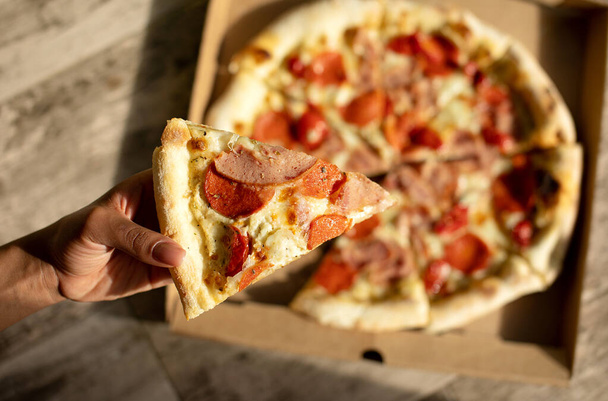hand taking piece of delicious pizza with ham, cheese and salami  - Foto, Imagem