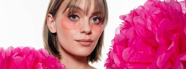 young woman with hydrogel eye patches near bright pink flowers isolated on white, banner - Foto, Imagen
