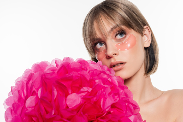 young woman with hydrogel eye patches looking away near bright pink flower isolated on white - Foto, Imagen