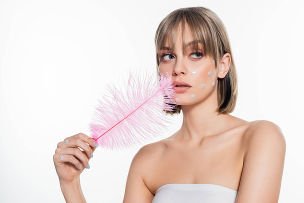 young woman with nacreous heart shape elements in makeup holding pink feather isolated on white  - Foto, Imagen