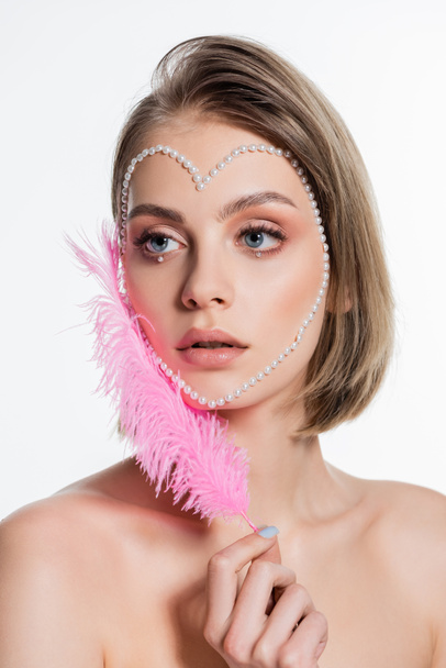 young woman with creative heart shape beads on face holding pink feather isolated on white  - Foto, immagini