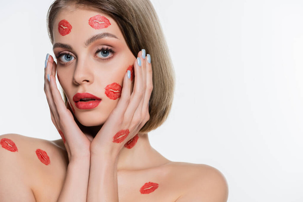 young woman with red kiss prints on cheeks touching face isolated on white - Fotoğraf, Görsel