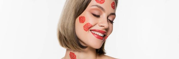 pleased young woman with red kiss prints on cheeks and body smiling isolated on white, banner - Фото, зображення