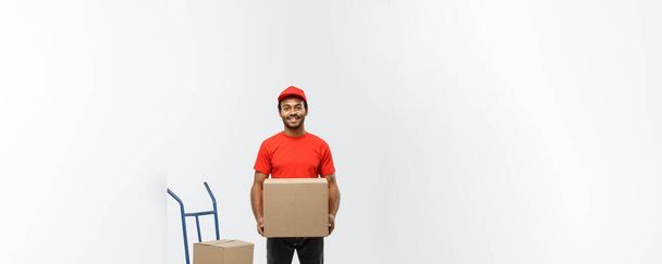 Delivery Concept - Portrait of Handsome African American delivery man or courier with hand truck and holding box. Isolated on Grey studio Background. Copy Space. - Photo, Image