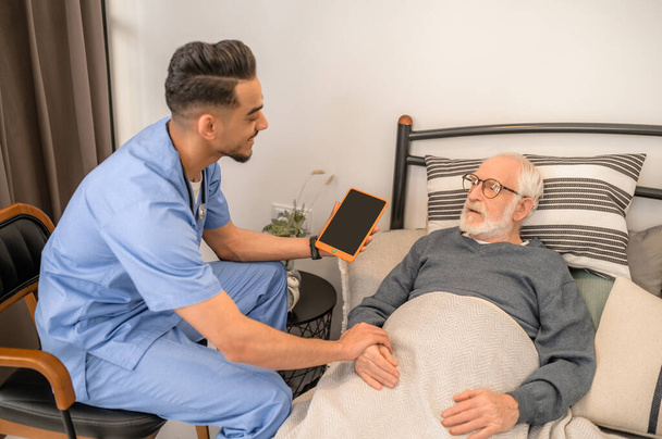 General practitioner examining a bedridden man during the home visit - Foto, afbeelding