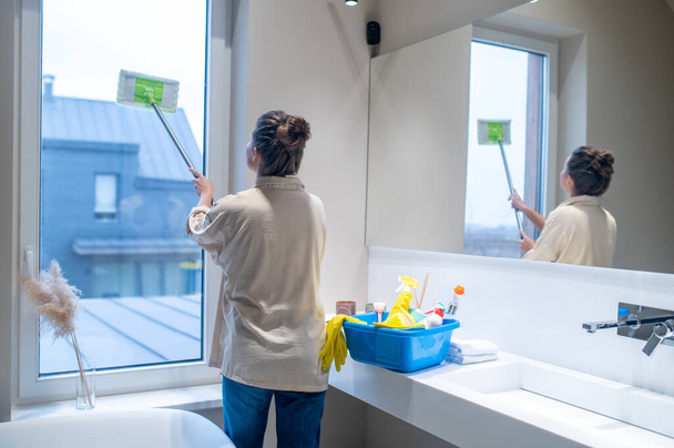 Young woman cleaning the window in the bathroom - Foto, afbeelding