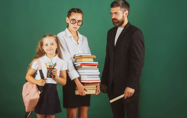 Portrait of father tutor and school kids daughters on green blackboard background. Reading book and writing. Dad teaching schoolchild girls in classroom. - Foto, Imagen