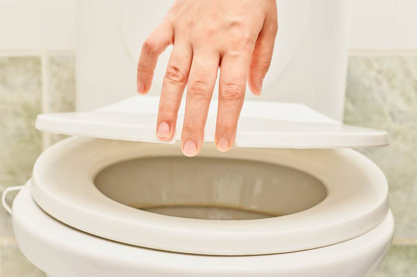 Рука людини, що відкриває кришку сидіння в туалеті
 - Фото, зображення