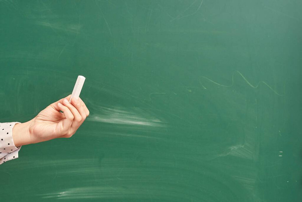 A teacher holding a piece of chalk over the green chalkboard - Foto, Bild