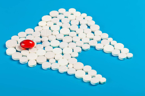 Tand gemaakt van witte pillen met een rode capsule op blauwe achtergrond - Foto, afbeelding