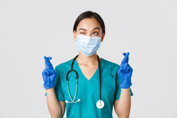 Covid-19 、コロナウイルス病、医療従事者の概念。医療用マスクと手袋の希望的なアジアの女性医師,左上隅を見て祈る,願いを作ります,白の背景 - 写真・画像