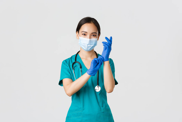 Covid-19, malattia coronavirica, concetto di operatore sanitario. Professionale e fiducioso sorridente medico asiatico, infermiera indossare guanti di gomma e maschera medica per l'esame del paziente, sfondo bianco - Foto, immagini