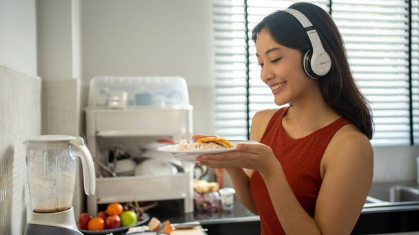 Piękna młoda kobieta gotująca w kuchni w domu słuchając muzyki przez słuchawki - koncepcje stylu życia - Zdjęcie, obraz
