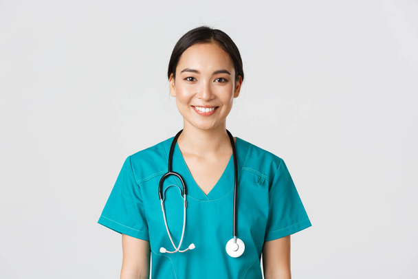Trabalhadores de saúde, prevenção de vírus, conceito de campanha de quarentena. Close-up de sorrir agradável asiático enfermeira feminina, médico em esfrega olhando otimista, ouvir paciente, fundo branco
 - Foto, Imagem