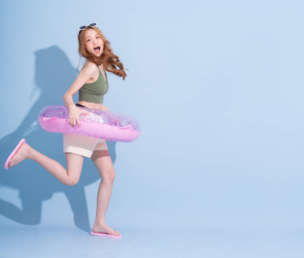 Image of young Asian girl holding swimming float on blue background, summer vacation concept - Zdjęcie, obraz