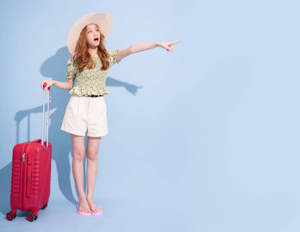 Imagen completa de la joven asiática con maleta sobre fondo azul, concepto de viaje - Foto, imagen