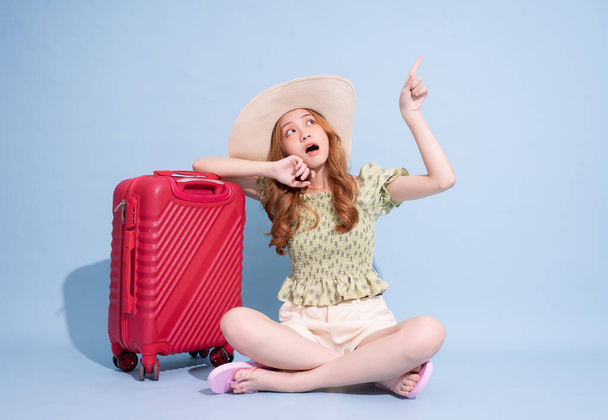 Повний образ молодої азіатської дівчини з валізою на синьому фоні. - Фото, зображення