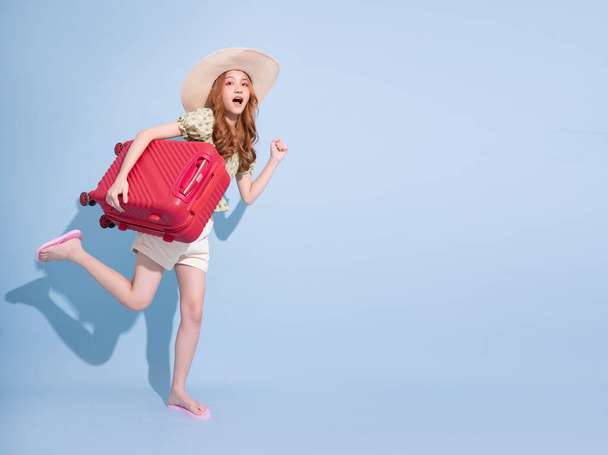 Image pleine longueur de jeune fille asiatique avec valise sur fond bleu, concept de voyage - Photo, image