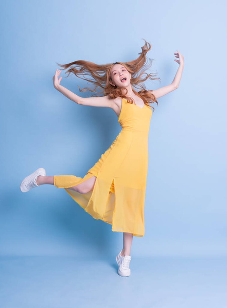 Full length image of young Asian woman wearing yellow dress on blue background - Φωτογραφία, εικόνα