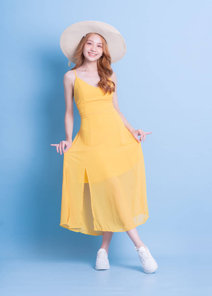 Full length εικόνα της νεαρής Ασιάτισσας που φοράει κίτρινο φόρεμα σε μπλε φόντο - Φωτογραφία, εικόνα