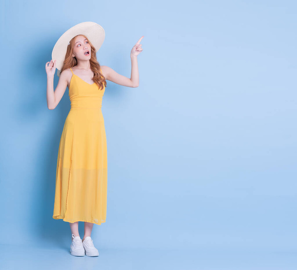 Full length image of young Asian woman wearing yellow dress on blue background - Foto, afbeelding