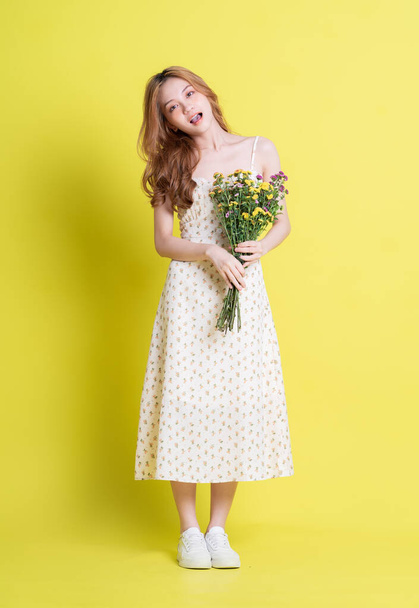Image of young Asian woman holding flowers on yellow background - Foto, Imagen