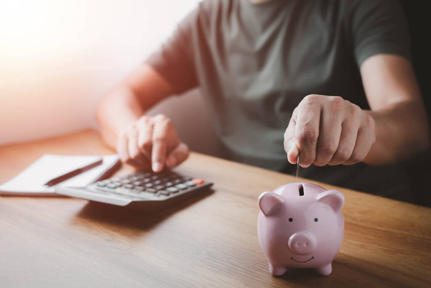 Ein Mann steckt Münzen in ein rosafarbenes Sparschwein, um Geld zu sparen. Planung vorantreiben, Geld sparen für Zukunftspläne, Altersvorsorge. Konzept der Unternehmensfinanzierung für die Buchführung. - Foto, Bild