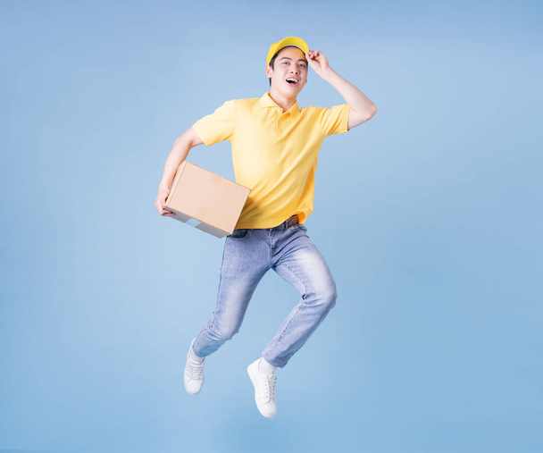 Full length image of Asian delivery man on blue background - Foto, imagen