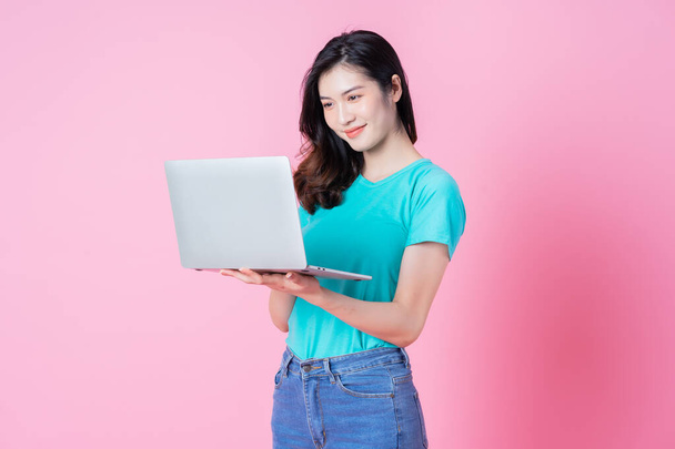 Young Asian woman using laptop on pink background - Fotó, kép