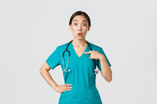 Covid-19, personnel de santé, concept pandémique. Surpris et embusqué asiatique femme médecin, infirmière dans les blouses pointant vers elle-même, beaing nommé ou choisi, debout fond blanc - Photo, image