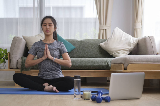 Young woman practicing yoga at home and watching online workout  lesson on laptop. Healthy lifestyle concept. - Foto, Imagen