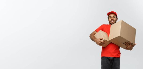 Toimitus Concept - Muotokuva Happy African American toimitus mies punaisella liinalla tilalla laatikko paketti. Eristetty Grey Studion taustalle. Kopioi tila. - Valokuva, kuva