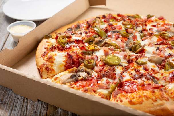 A view of a jalapeno and meat pizza in a delivery box. - Zdjęcie, obraz