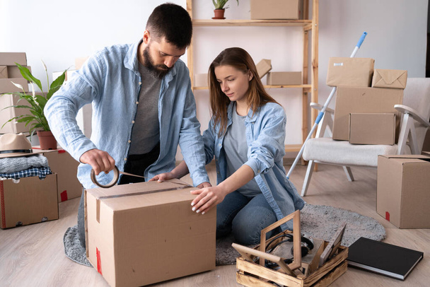 A man and a woman pack things on the day of the move. the guy seals the cardboard box with tape. copy space. - Photo, Image
