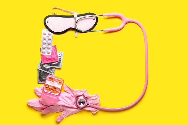 Rahmen aus Pillen, Kondomen, Stethoskop, Handschuhen und Augenbinde auf gelbem Hintergrund - Foto, Bild