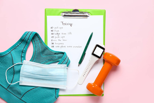 Clipboard with training, sport top, medical mask and smartwatch on pink background - Fotografie, Obrázek