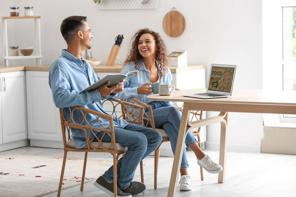 Happy young couple using modern laptop in kitchen - Photo, Image