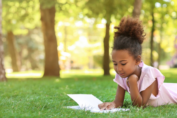 Little African-American girl reading book on grass in park - Photo, Image