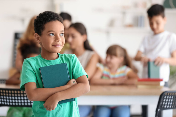 Kleiner afroamerikanischer Junge mit Buch im Klassenzimmer - Foto, Bild
