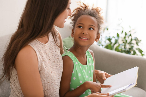 Klein Afrikaans-Amerikaans meisje lezen boek met haar leraar op de bank - Foto, afbeelding